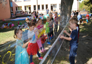dzieci malują farbami na folii zawieszonej między drzewami w ogrodzie